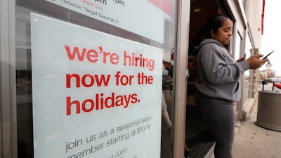 In this Nov. 27, 2019 photo, a passer-by walks past a hiring for the holidays sign near an entrance to a Target store location, in Westwood, MA.