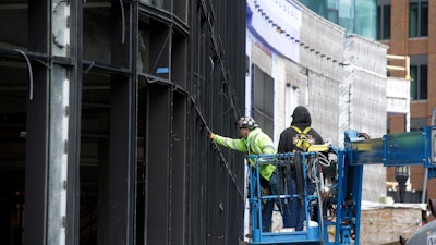 In this Nov. 27, 2019 photo, workers use a lift while working on a new building in Boston's Seaport district.