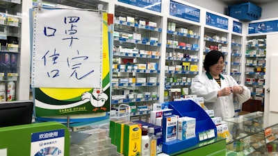 In this Tuesday, Jan. 21 file photo, pharmacist Liu Zhuzhen stands near a sign reading 'face masks are sold out' at her pharmacy in Shanghai, China. Panic and pollution drive the market for protective face masks, so business is booming in Asia, where fear of the virus from China is straining supplies and helping make mask-wearing the new normal.