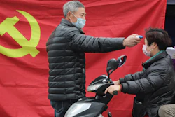 A volunteer stands in front of a Communist Party flag as he takes the temperature of a scooter driver at a roadside checkpoint in Hangzhou in eastern China's Zhejiang Province on Monday, Feb. 3.