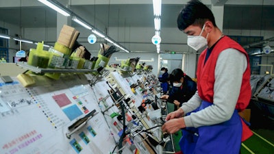 In this Feb. 13 photo, masked workers assembly wiring for automobile at a factory in Qingdao in east China's Shandong province. Automakers are gradually reopening factories in China that were idled by anti-virus controls as they try to reverse a sales slump in their biggest market.