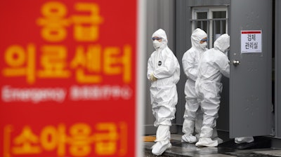 Officials wearing protective attire work to diagnose people with suspected symptoms of the new coronavirus at a hospital in Daegu, South Korea on Wednesday, Feb. 26. The number of new virus infections in South Korea jumped again Wednesday and the U.S. military reported its first case among its soldiers based in the Asian country, with his case and many others connected to a southeastern city with an illness cluster. A sign reads 'Emergency Medical Center.'