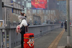 A traveler stands on a bridge near a display showing government propaganda in the fight against the COVID-19 viral illness in Beijing, China Thursday, Feb. 13, 2020. China is struggling to restart its economy after the annual Lunar New Year holiday was extended to try to keep people home and contain novel coronavirus. Traffic remained light in Beijing, and many people were still working at home.