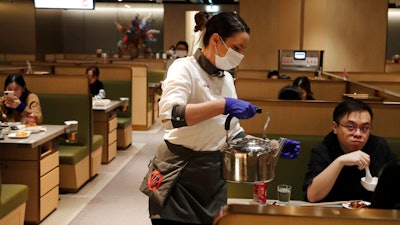 In this March 5, 2020, photo, a waitress of the Chinese restaurant Hot Pot serves customers in London.