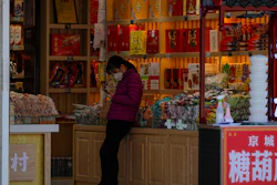 In this Tuesday, March 10, 2020, a staff wearing a protective mask browses her smartphone while waiting for customers at a shop at the Wangfujing shopping district following the coronavirus outbreak in Beijing.