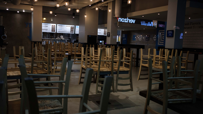 In this March 16, 2020 file photo, chairs hang stacked on empty tables at a closed restaurant in New York.