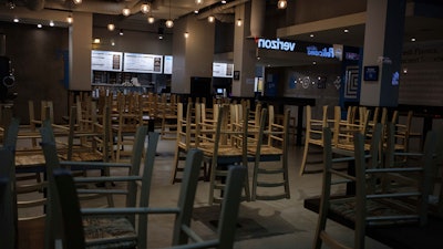 In this March 16, 2020 file photo, chairs hang stacked on empty tables at a closed restaurant in New York.