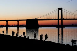 People gather to watch the sun set behind the Throgs Neck Bridge at LIttle Bay Park Wednesday, April 8, 2020, in the Queens borough of New York. While New York Gov. Andrew Cuomo said New York could be reaching a 'plateau' in hospitalizations, he warned that gains are dependent on people continuing to practice social distancing.