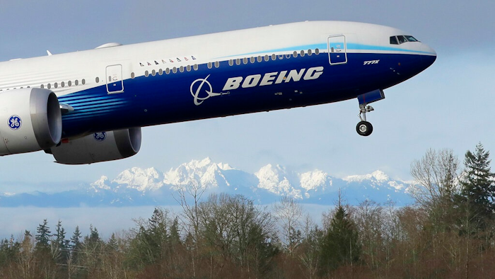 In this Jan. 25, 2020, file photo a Boeing 777X airplane takes off on its first flight with the Olympic Mountains in the background at Paine Field in Everett, Wash. Boeing on Wednesday, May 27, is cutting more than 12,000 jobs through layoffs and buyouts as the coronavirus pandemic seizes the travel industry. And the aircraft maker says more cuts are coming.