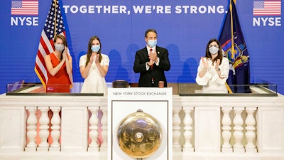 In this image provided by the New York Stock Exchange, New York State Gov. Andrew Cuomo, center, applauds as he rings the opening bell of the New York Stock Exchange with with New York Stock Exchange President Stacey Cunningham, right on Tuesday, May 26 in New York. The NYSE allowed a limited number of traders back to the floor with social distancing guidelines and face masks.