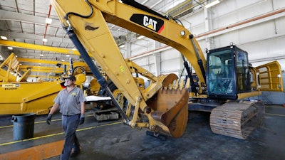 In this Sept. 18, 2019, photo a Puckett Machinery Company technician walks past a new heavy duty Caterpillar excavator that awaits modification at Puckett Machinery Company in Flowood, Miss. Caterpillar is reporting a third-quarter profit of $668 million and topped most expectations, though demand for its equipment is being driven down by the pandemic. The Deerfield, Illinois, company reported a profit Tuesday, Oct. 27, 2020, of $1.22 per share.