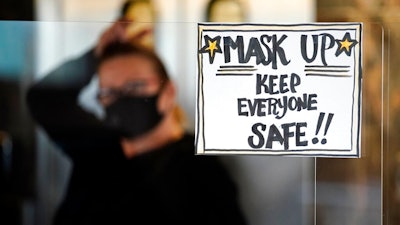 In this Tuesday, Nov. 17, 2020 file photo, manager Yllka Murati waits for a delivery driver to pick up takeout orders behind a partition displaying a sign to remind customers to wear a mask, at the Penrose Diner, in south Philadelphia.
