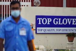 A worker from Top Glove walks outside Top Glove factory in Shah Alam, Malaysia, Wednesday, Nov. 25, 2020. Malaysia's Top Glove Corp., the world's largest maker of rubber gloves, says it expects a two to four-week delay in deliveries after more than 2,000 workers at its factories were infected by the coronavirus, raising the possibility of supply disruptions during the pandemic.