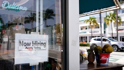 A 'Now Hiring,' sign is shown in the window of a restaurant in Miami Beach, Fla. America's employers likely cut back on hiring last month, and may have even shed jobs, as the economy suffers from a resurgent virus.