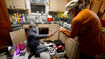In this Feb. 20 photo, Handyman Roberto Valerio, left, hands homeowner Nora Espinoza the broken pipe after removing it from beneath her kitchen sink in Dallas. The pipe broke during freezing temperatures brought by last week's winter weather.
