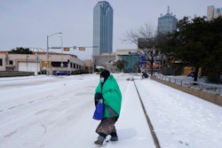 In this Feb. 16, 2021, file photo, a woman wrapped in a blanket crosses the street near downtown Dallas. As temperatures plunged and snow and ice whipped the state, much of Texas' power grid collapsed, followed by its water systems. Tens of millions huddled in frigid homes that slowly grew colder or fled for safety.