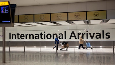 Passengers walk past a sign in the arrivals area at Heathrow Airport, London, Jan. 26, 2021.