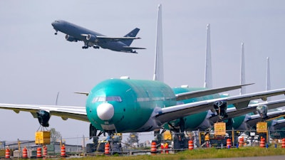 In this April 23 photo, a U.S. Air Force KC-46A Pegasus jet takes off in view of a line of Boeing 777X jets parked nose to tail on an unused runway at Paine Field, near Boeing's massive production facility in Everett, Wash.