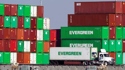 Shipping containers are stacked over a truck at the Port of Los Angeles Wednesday, Nov. 10, 2021, in Los Angeles. One month after President Joe Biden announced an agreement to have the Port of Los Angeles operate round-the-clock to help break a cargo backlog at the docks, officials disclose that hasn’t happened as they contend with a shortage of truck drivers and accessible warehouse space.