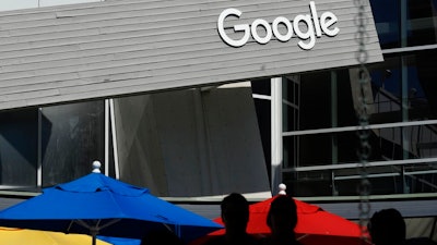 People walk by a Google sign on the company's campus in Mountain View, Calif., on Sept. 24, 2019. Google and Ford Co. are among those once again delaying their return-to-office plans, while other businesses whose workers are already back to the office are considering adding extra precautions like masks and doing COVID-19 testing.