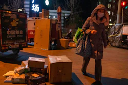 A woman wearing a mask to protect from the coronavirus walks past parcels gathered near delivery tricycles in Beijing, China, Tuesday, Jan. 18, 2022. Chinese state media say parcels mailed from overseas may have spread the omicron variant of the coronavirus in Beijing and elsewhere, despite doubts among overseas health experts that the virus can be transmitted via packaging.