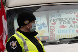 A police officer walks among protest vehicles as he distributes notices to protesters, Wednesday, Feb. 16, 2022 in Ottawa.