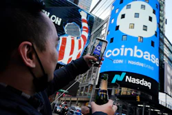 Coinbase employee Daniel Huynh holds a celebratory bottle of champagne as he photographs outside the Nasdaq MarketSite, Times Square, New York, April 14, 2021.
