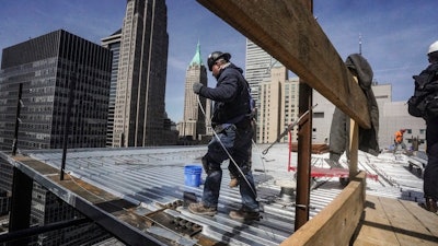 Construction workers install roofing on a high rise in Manhattan's financial district on Tuesday, April 11, 2023, in New York. On Friday, the U.S. government issues the April jobs report.