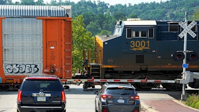 Cars wait at a railroad crossing for a CSX freight train in Homestead, Pa., June 18, 2023.