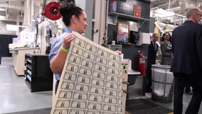 A worker carries a sheet of newly printed U.S. dollar bills at the Bureau of Engraving and Printing's Western Currency Facility, Fort Worth, Texas, Dec. 8, 2022.