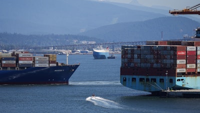 A boater passes between cargo ships on the harbor in Vancouver, British Columbia, July 16, 2024.