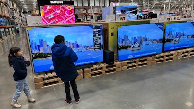 Young shoppers look over a row of large-screen televisions in a Costco warehouse, Denver, Dec. 19, 2024.