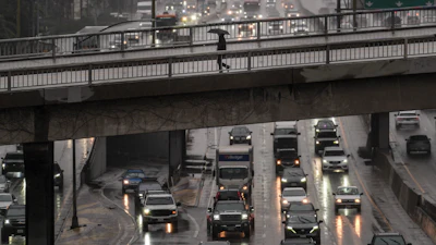 A pedestrian with an umbrella walks on a bridge over the rain-soaked 110 Freeway in Los Angeles, Nov. 14, 2025.