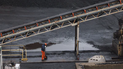 Industrial worker in orange safety gear near elevated conveyor belt at manufacturing site