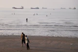 Men walk on the shoreline as people wade in the water in the Strait of Hormuz off Bandar Abbas, Iran, June 1, 2026.