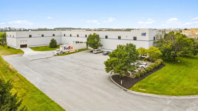 Large industrial warehouse facility with FedEx delivery truck in parking lot surrounded by manicured landscaping