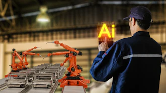 Industrial worker in blue uniform monitoring robotic arms on factory assembly line with glowing AI symbol