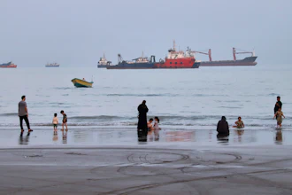 People spend time at a beach as commercial vessels are anchored in the Strait of Hormuz off Bandar Abbas, Iran, Aug. 5, 2026.