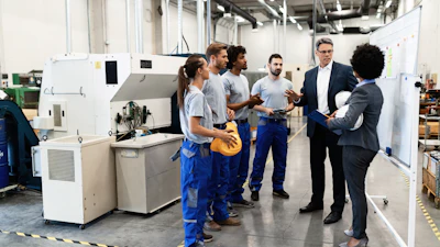 Manufacturing facility tour with workers and business professionals discussing near industrial machinery