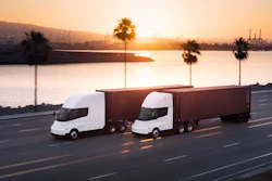 Two white autonomous semi-trucks with cargo containers driving on a highway at sunset with a port and palm trees in the background