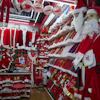 Christmas market stall displaying red Santa costumes, white fur trim, and holiday decorations with a young shopper browsing merchandise.
