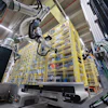 Robotic automation system with mechanical arms operating above yellow storage racks in an industrial warehouse facility