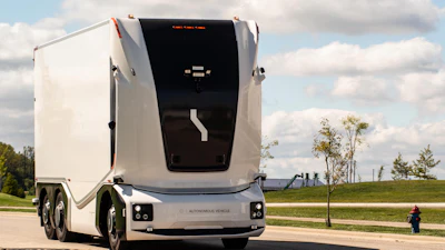 White autonomous semi-truck with black cabin parked on a paved road with green fields and cloudy sky in background