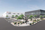Architectural rendering of modern office and industrial facility with white and gray buildings, desert landscaping, parking area, and people in courtyard.