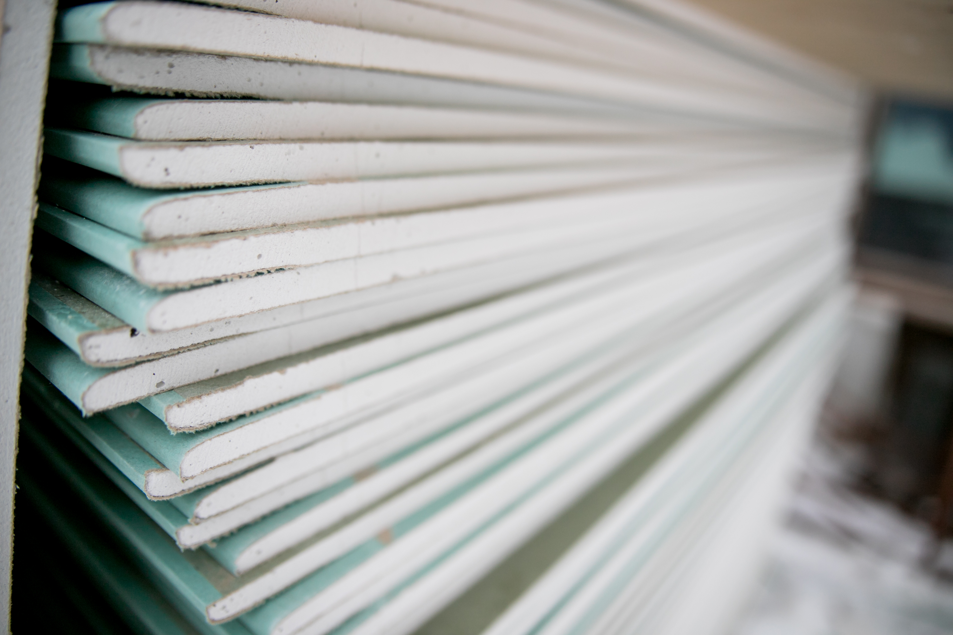 Close-up view of stacked drywall sheets showing white and teal-tinted edges layered together