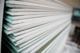Close-up view of stacked drywall sheets showing white and teal-tinted edges layered together
