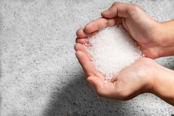 Hands holding white salt or sugar crystals against concrete background