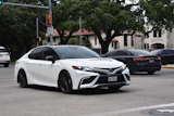 White Toyota Camry sedan parked on urban street with trees and buildings in background