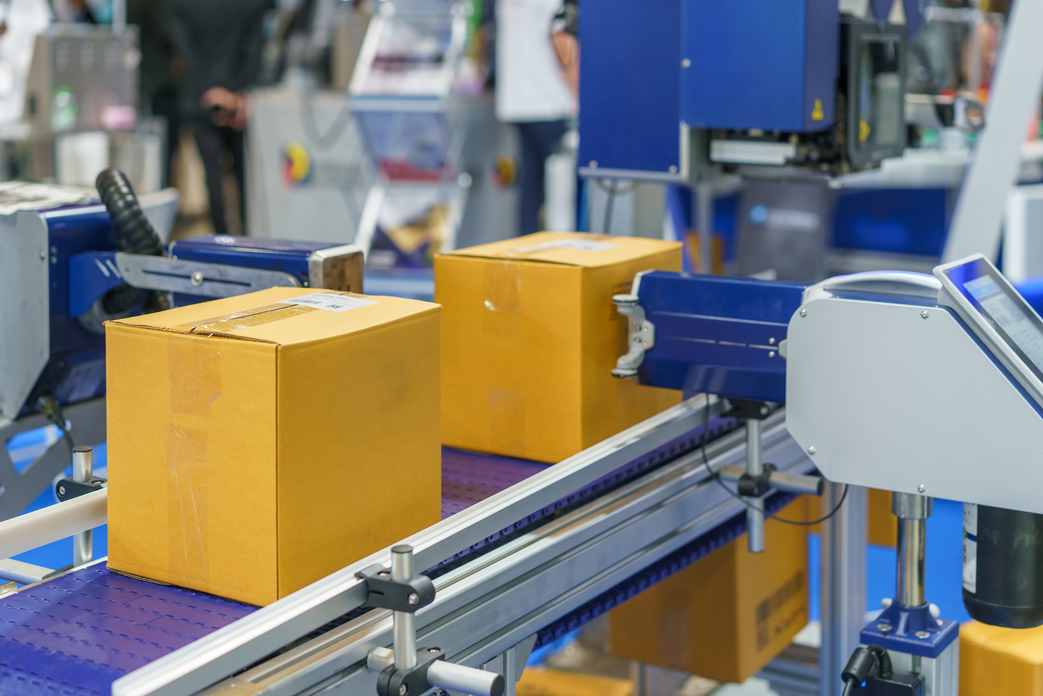 Yellow cardboard boxes moving on industrial conveyor belt in packaging facility with blue machinery
