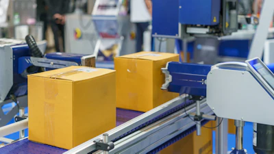 Yellow cardboard boxes moving on industrial conveyor belt in packaging facility with blue machinery